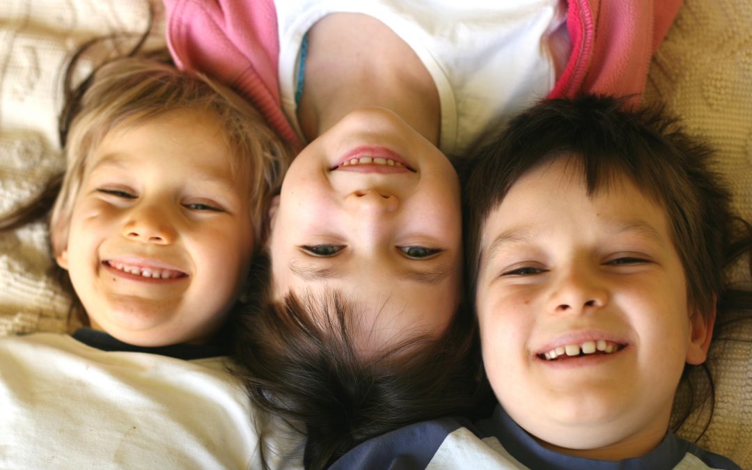 Three smiling children laying with their heads together