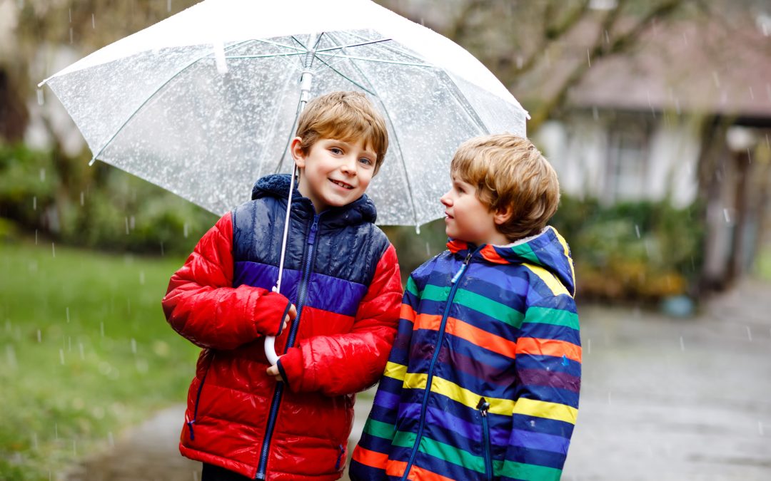 wo little kid boys on way to school walking during sleet, rain and snow with umbrella on cold day. Children, best friends and siblings in colorful fashion casual clothes