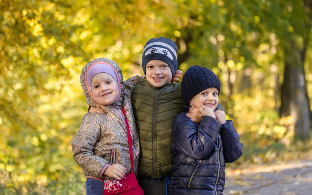 Group of happy three kids having fun outdoors in autumn park. Cute children enjoy hugging together against golden fall background. Best frend forever and happy childhood concept